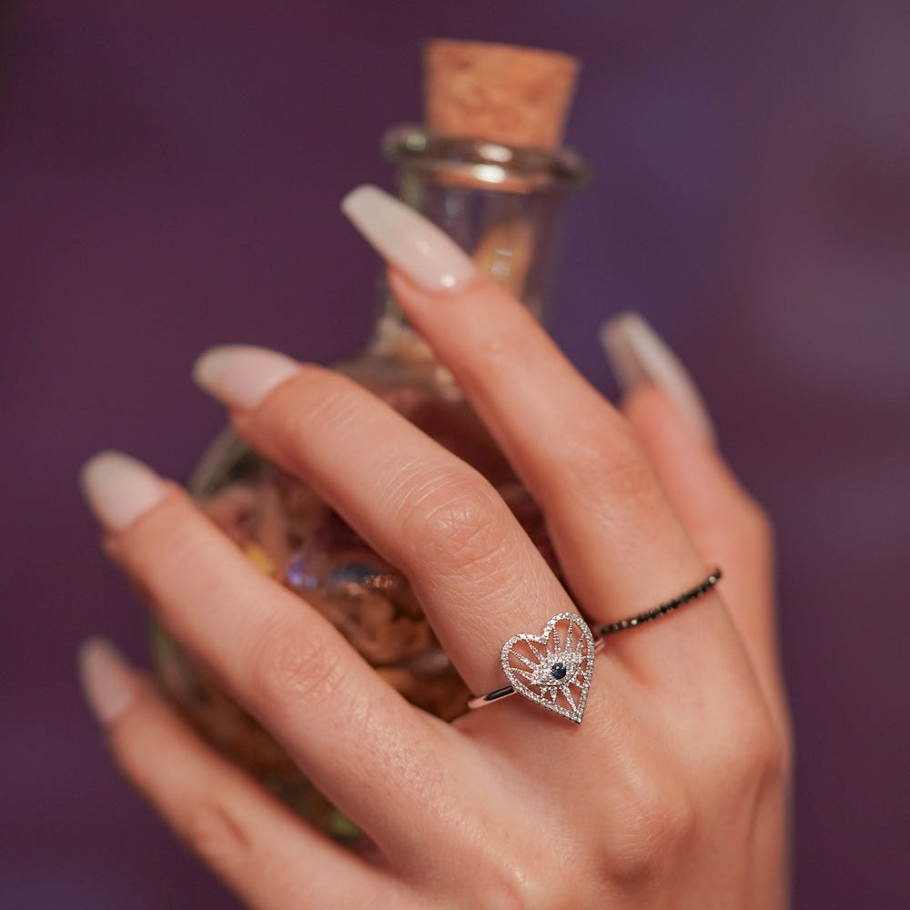 Hand holding a small bottle with a heart-shaped ring on a blurred background