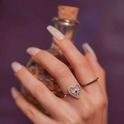 Hand holding a small bottle with a heart-shaped ring on a blurred background