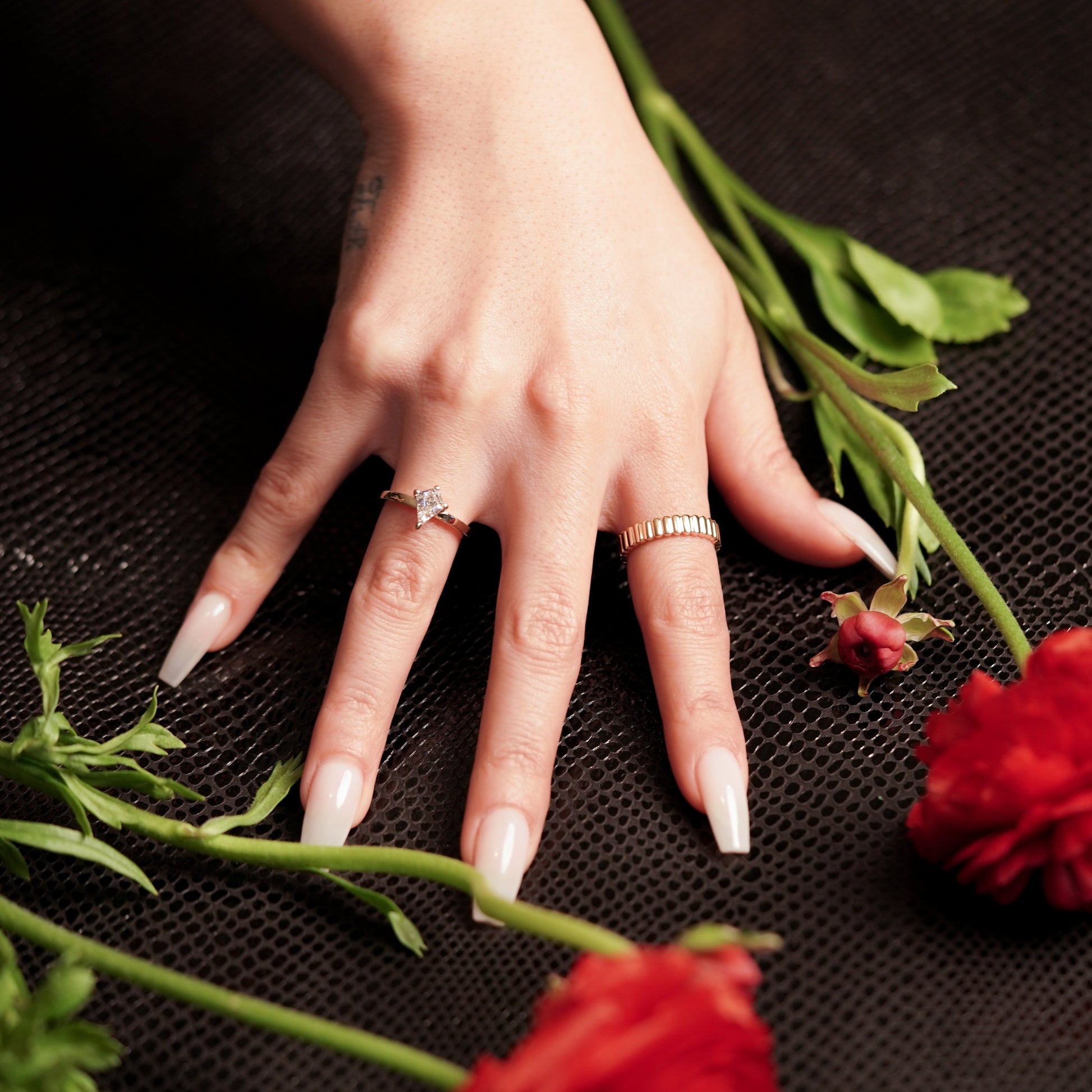 Hand with rings on a black surface with red flowers
