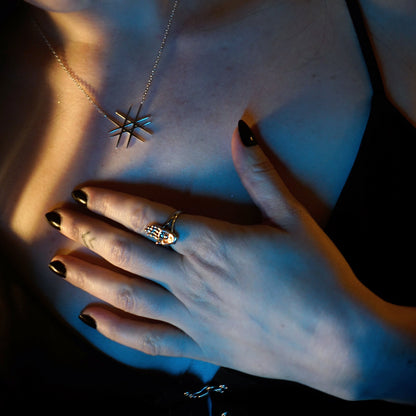 Close-up of a person wearing a geometric-shaped necklace and silver ring with a dark background