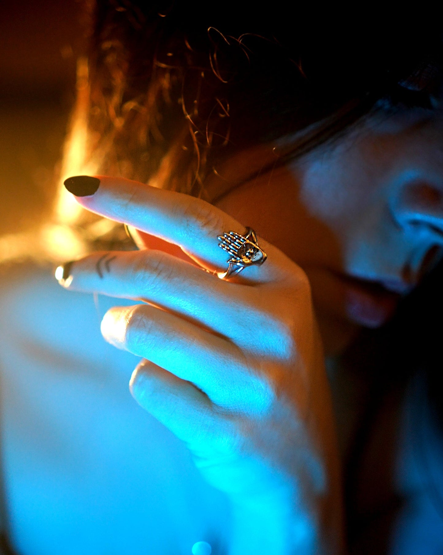 Close-up of a hand with a ring and painted nails against a blurred background