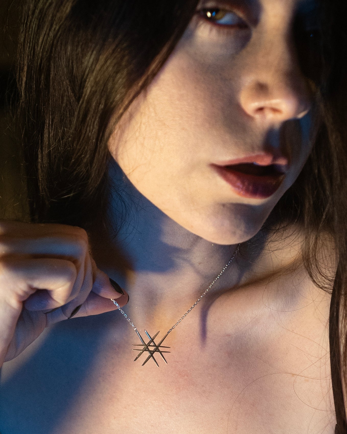 Roniit wearing a geometric-shaped necklace with a soft light on her face