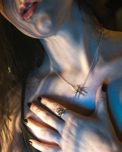 Close-up of a person wearing a geometric-shaped necklace with a hand resting on their chest.